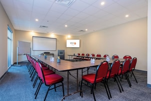 Een vergaderruimte met een lange tafel, rode stoelen, een whiteboard en een projectorscherm waarop 'SPOT HOTEL ORLANDO' staat.