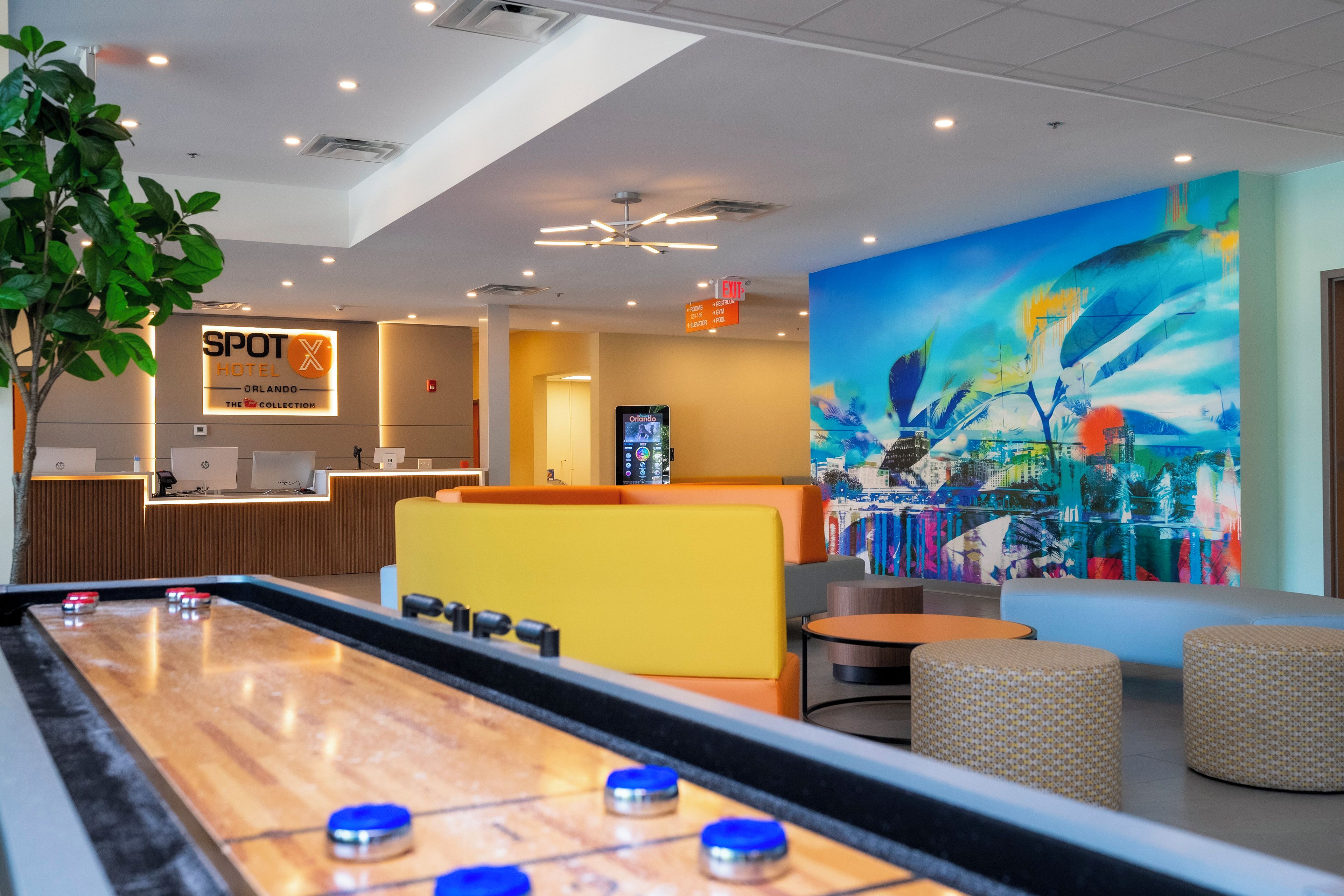 A pool table in a hotel lobby with a reception desk, seating area, and a large abstract painting.