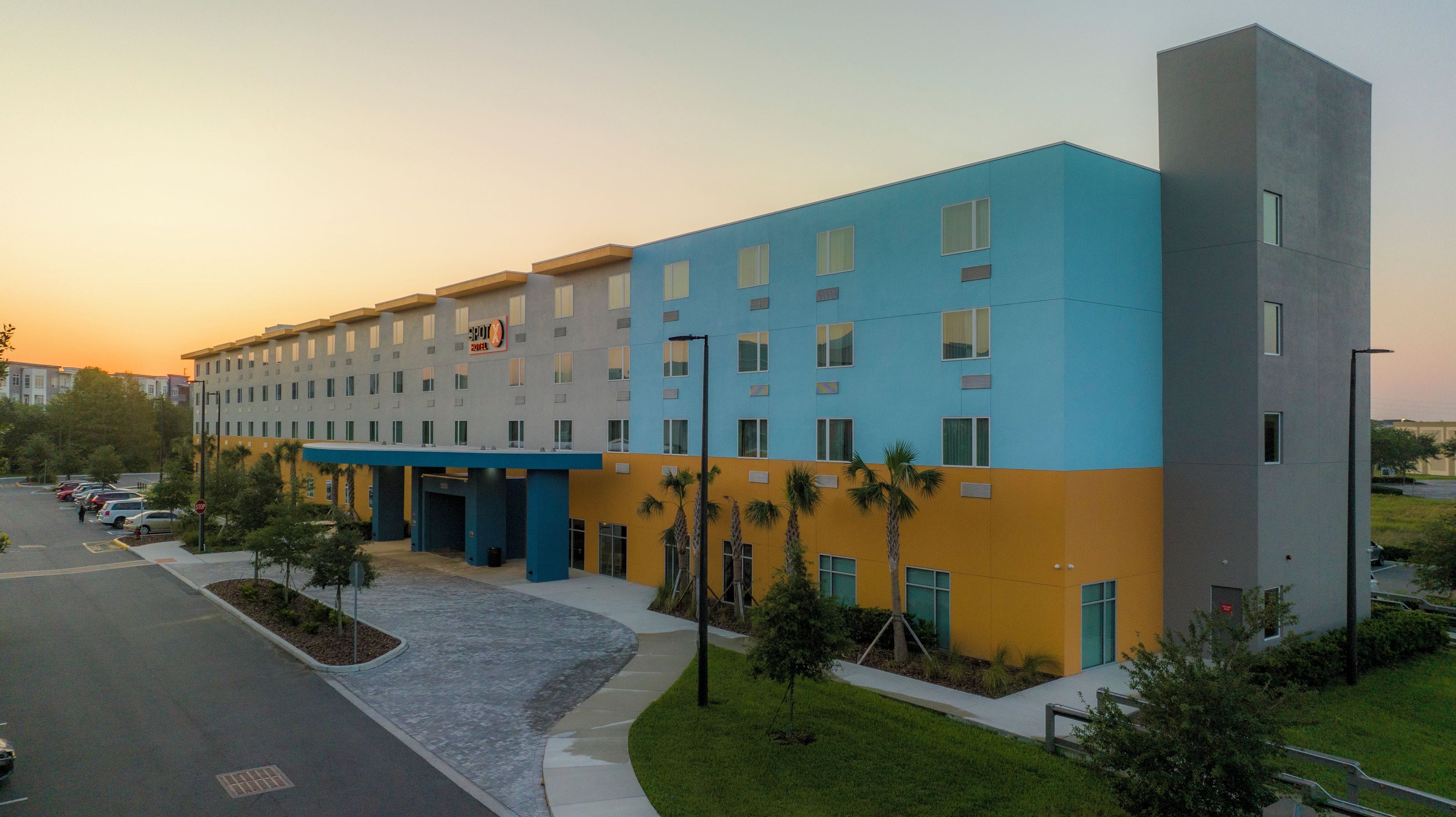 Een hotel met meerdere verdiepingen, een blauwgele gevel, een parkeerplaats en een voetpad.