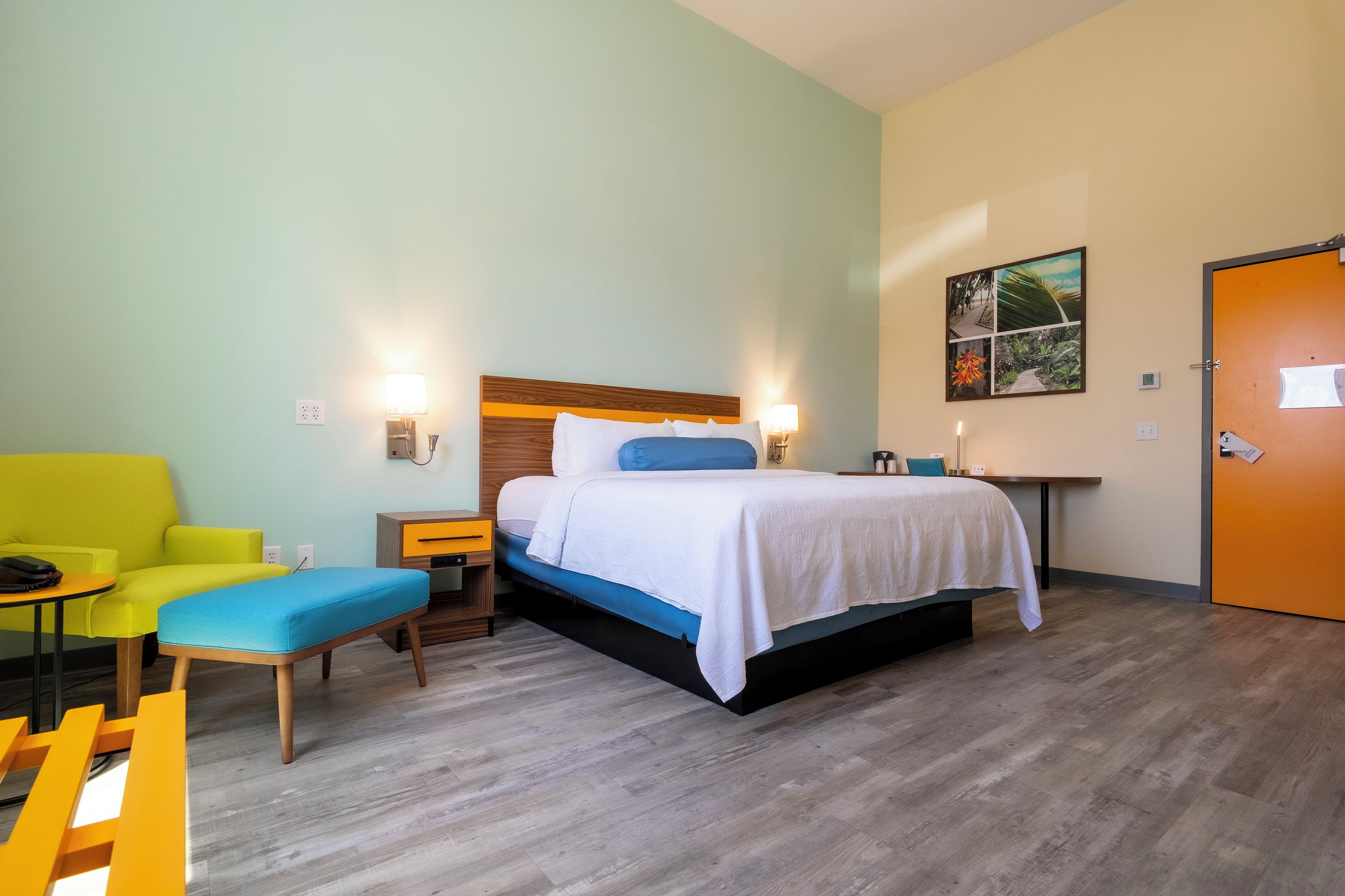 A hotel room with a bed, bedside tables, a chair, a desk, and a door.