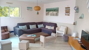 A modern living room with a sectional sofa, a coffee table, a TV, and a bookshelf. - Villa 12 pers : 6 bedrooms, 3 bathrooms, 3wc/ 200m from the beach of La Sauzaie (Bretignolles-sur-Mer)