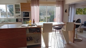 A modern kitchen with a central island, a dining area with bar stools, and a view of greenery outside. - Villa 12 pers : 6 bedrooms, 3 bathrooms, 3wc/ 200m from the beach of La Sauzaie (Bretignolles-sur-Mer)