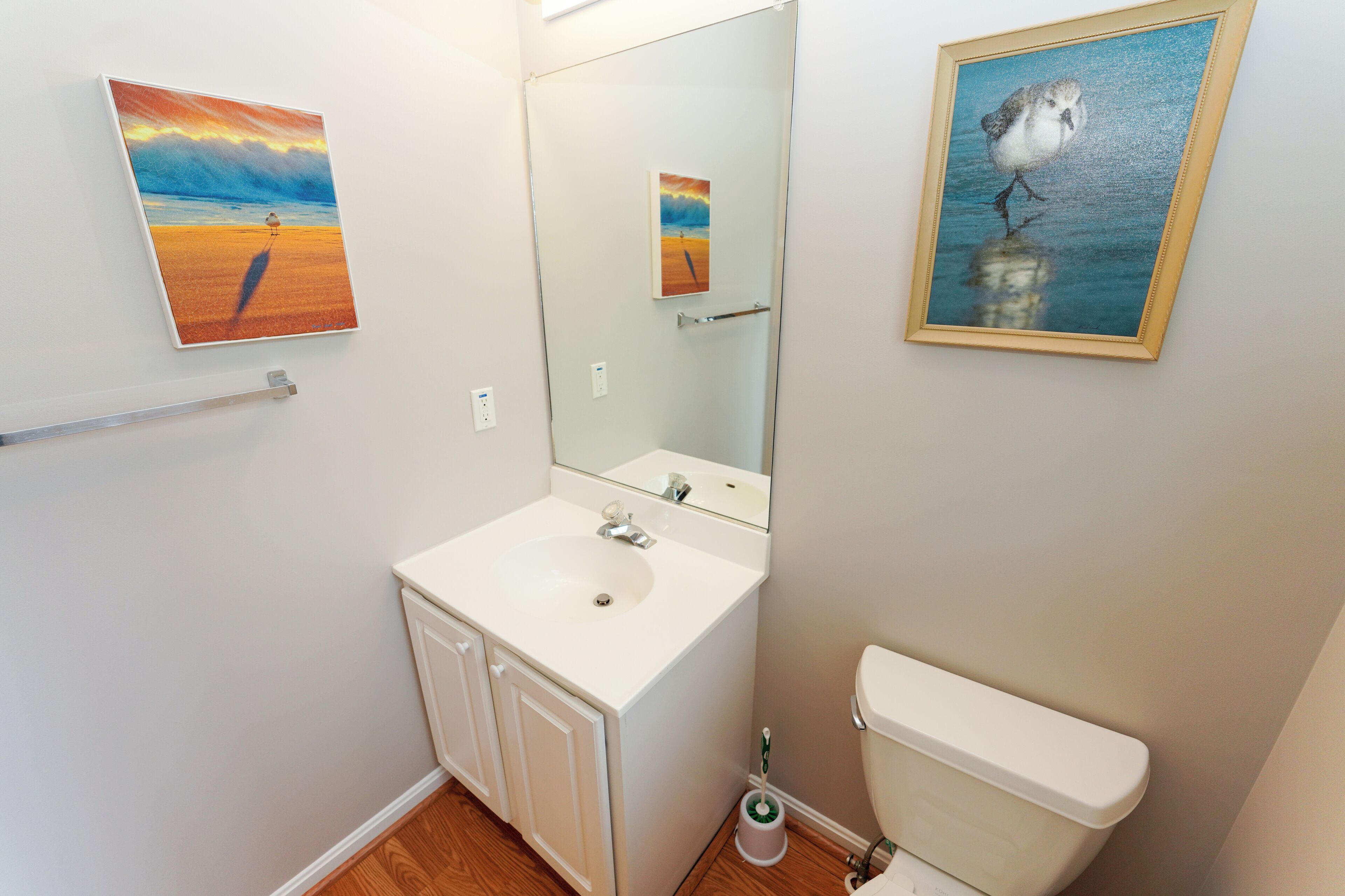 12 Dune Road - Tower Shores - Half Bathroom Details - A clean and modern half-bathroom featuring a crisp white vanity, mirror, and coastal artwork.