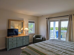 A bedroom with a bed, a dresser, a TV, two lamps, a chair, and a balcony with a view. - Oceanfront 4BR Duplex in Bethany Beach – Panoramic Views & Private Beach Access (Fenwick Island)