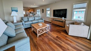 A spacious living room with a sectional sofa, a coffee table, and a TV on a wooden stand. - Oceanfront 4BR Duplex in Bethany Beach – Panoramic Views & Private Beach Access (Fenwick Island)