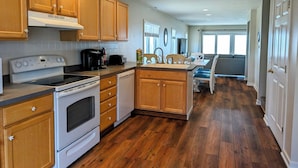 A kitchen with wooden cabinets, a stove, and a dishwasher. There is a dining area with a table and chairs. - Oceanfront 4BR Duplex in Bethany Beach – Panoramic Views & Private Beach Access (Fenwick Island)