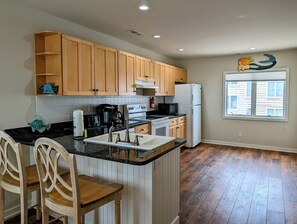 38901 Bunting Avenue Kitchen Island with Bar Seating and Hardwoo - A perspective of the kitchen featuring a central island with white lattice-back barstools and a view toward the bright dining area. - Oceanfront 5BR Duplex in Fenwick Island – Direct Beach Access & Stunning Views (Fenwick Island)