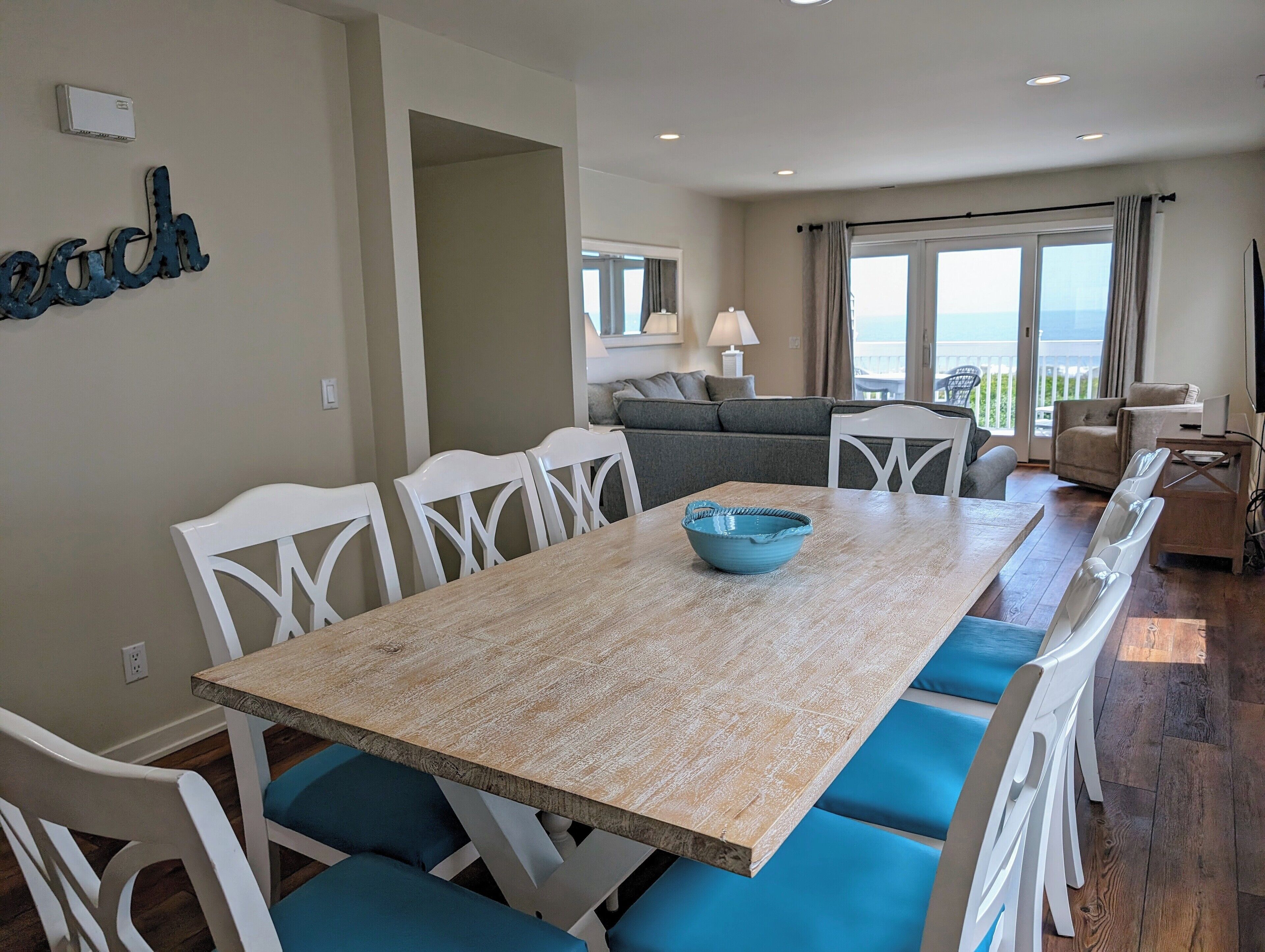 38901 Bunting Avenue Dining Table and Beach Decor - A view of the dining space highlighting the large wooden table and a "beach" decorative sign on the wall, leading into the open living area.