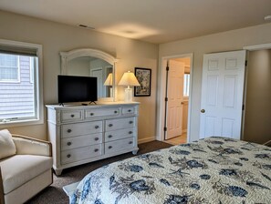 289A - 38901 Bunting Avenue Master Bedroom Perspective with Whit - A view of the master bedroom highlighting the large white dresser with a mirror and TV, an upholstered beige armchair, and the entry door to the room. - Oceanfront 5BR Duplex in Fenwick Island – Direct Beach Access & Stunning Views (Fenwick Island)