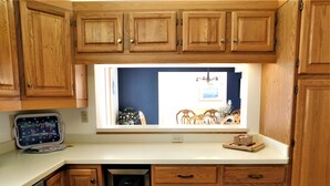 A kitchen with wooden cabinets, a built-in dishwasher, a window with a view of a dining area, and a small countertop with a tray. - Spacious 6BR Family Home – Just 3 Blocks to Bethany Beach in The Canal Community (Bethany Beach)