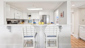 Cozinha moderna com armários brancos, uma ilha central com banquetas e uma geladeira de aço inoxidável.