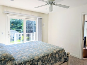 A bedroom with a bed, a ceiling fan, and a sliding glass door leading to a balcony.