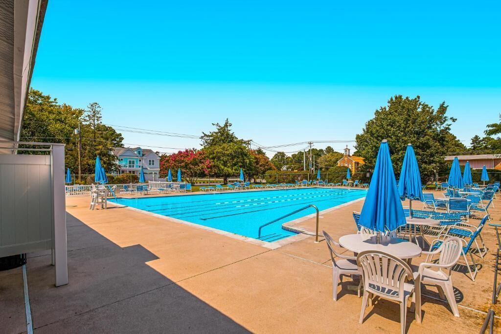 A swimming pool with lounge chairs and umbrellas, surrounded by trees and buildings.