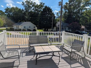 A deck with four chairs and a table, surrounded by a white fence, overlooking a residential area with houses and trees.