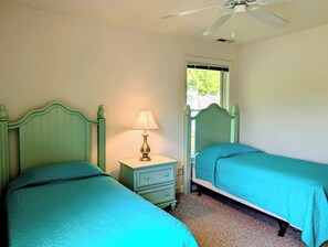 A bedroom with two single beds, a nightstand with a lamp, a ceiling fan, and a window.