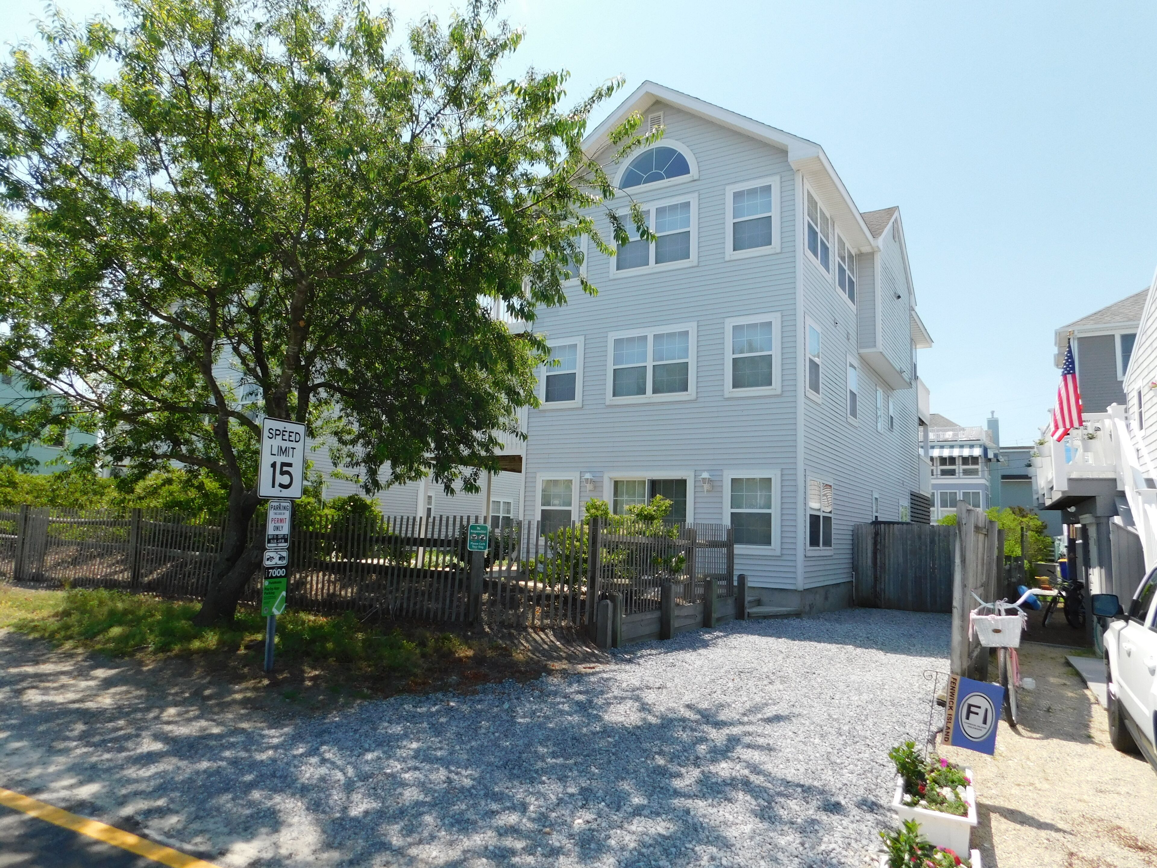 6 South Carolina Avenue - Side Yard and Exterior Profile - Mature trees and fencing wrap around the property, offering a sense of seclusion in the heart of Fenwick Island. The home's light-colored siding and traditional beach-style architecture blend perfectly with the surrounding coastal neighborhood.