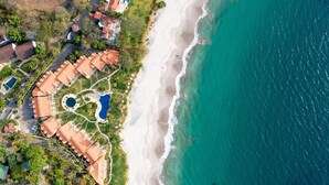 Oversigtsbillede af et kystresort med flere bygninger, en strand og en swimmingpool.