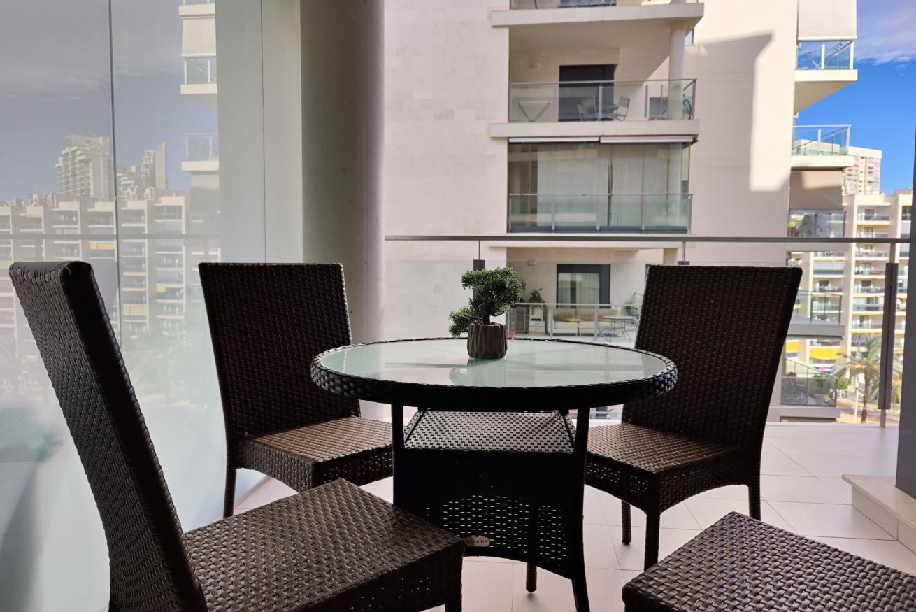 Ein Balkon mit Korbstühlen und einem Glastisch, mit Blick auf eine Stadtansicht.