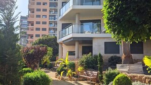 Un edificio residencial de varios pisos con balcones, rodeado de jardines bien cuidados y un camino pavimentado.