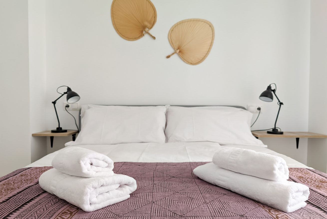 Una cama bien hecha con sábanas blancas, dos lámparas de noche y una colcha estampada.