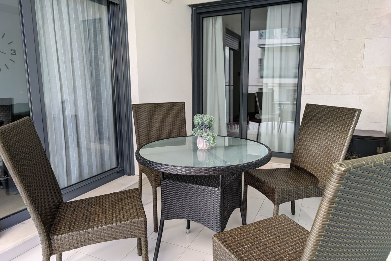 A round glass table with wicker chairs, a potted plant, and a sliding glass door.