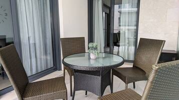 A round glass table with wicker chairs, a potted plant, and a sliding glass door.