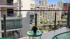 Un balcón con una mesa de vidrio, una planta en maceta y vistas a la ciudad.