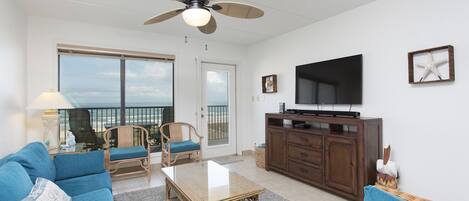 A spacious living room with a large window, a ceiling fan, a flat-screen TV, and a wooden cabinet.