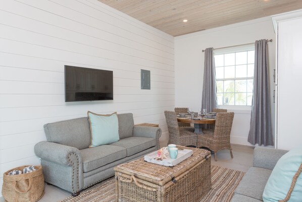 A cozy living room with a grey sofa, wicker coffee table, and a television mounted on the wall.