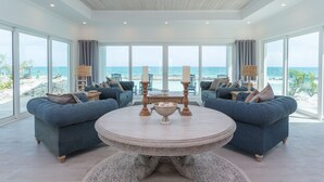 A spacious living room with a large round table, two sofas, and a view of the beach.