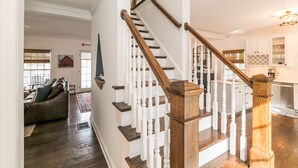 Una escalera con balaustres de madera y barandilla, que conduce a una zona de cocina con armarios blancos y una mesa de comedor.