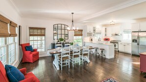 Amplia sala de estar con una mesa de comedor, sillas rojas y un área de cocina con armarios blancos y electrodomésticos de acero inoxidable.