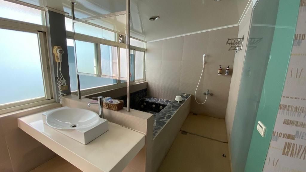 A modern bathroom with a large window, a standalone sink, a shower area, and a vanity with a mirror.