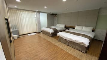A hotel room with two beds, a wooden floor, a large window with curtains, and a small bedside table.