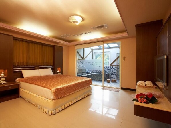 A hotel room with a bed, a desk, a TV, and a sliding glass door leading to an outdoor area.