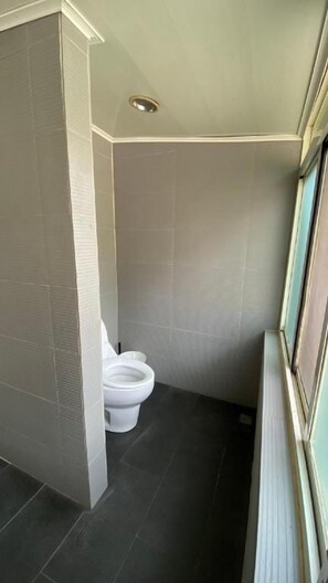 A bathroom with a toilet, tiled walls, and a window. - Kylin Peak Hotspring Resort (Taichung)