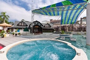 En swimmingpool med jacuzzi, overdækket siddeplads og et vandfald.