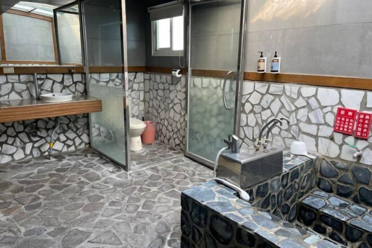A bathroom with stone flooring, a wooden vanity, a glass shower enclosure, and a toilet.