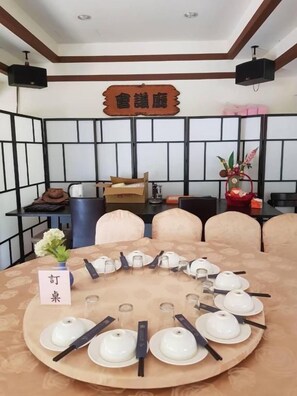 Une salle de conférence avec une table ronde préparée pour une réunion, équipée de porte-noms, de théières et de baguettes.