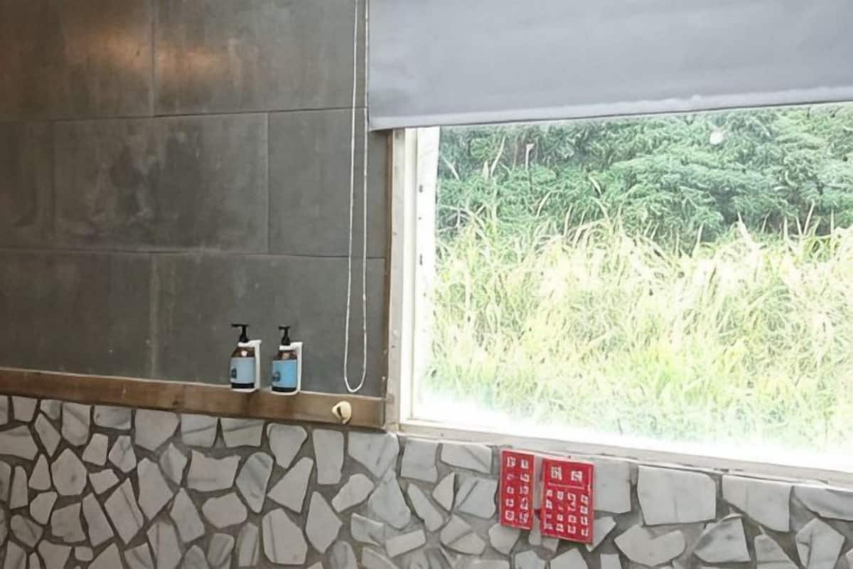 A bathroom with a stone wall, a window with a view of greenery, and two soap dispensers on the wall.