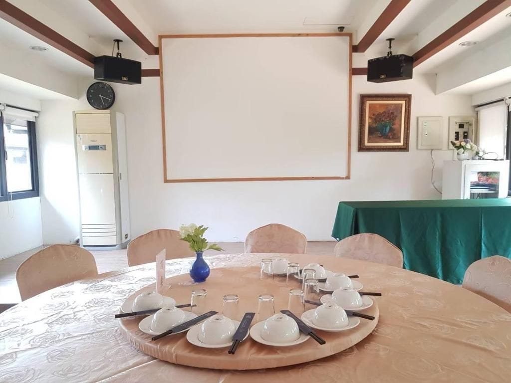 A conference room with a round table set for a meeting, a projector screen, and a clock on the wall.