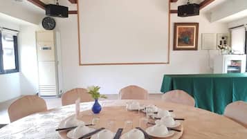 A conference room with a round table set for a meeting, a projector screen, and a clock on the wall.