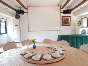 A conference room with a round table set for a meeting, a projector screen, and a clock on the wall.