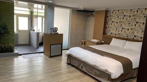 A hotel room with a bed, a desk, a small cabinet, a shower area, and a wall with patterned wallpaper.