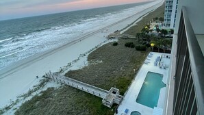 A high-rise hotel overlooking a beach with a swimming pool and a boardwalk.