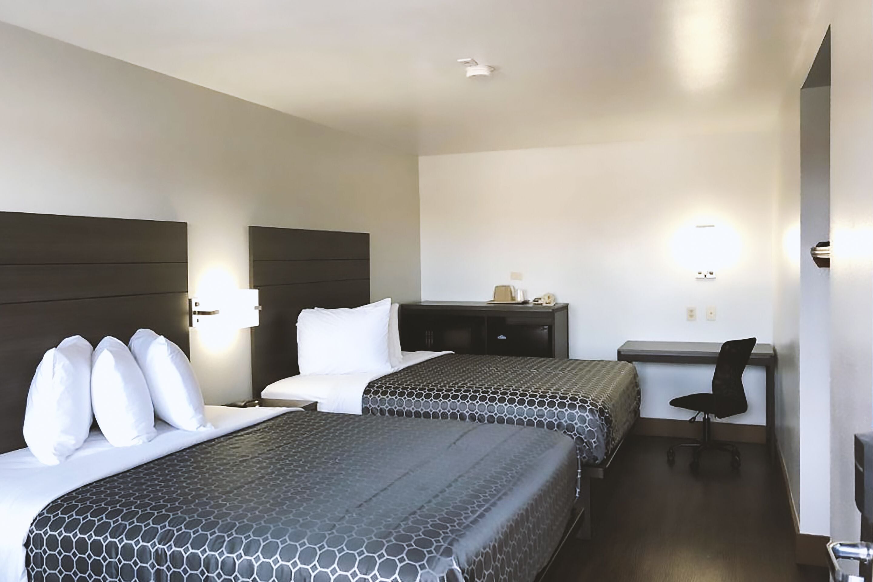 Una habitación de hotel con dos camas, un escritorio, una silla y una mesita de noche.