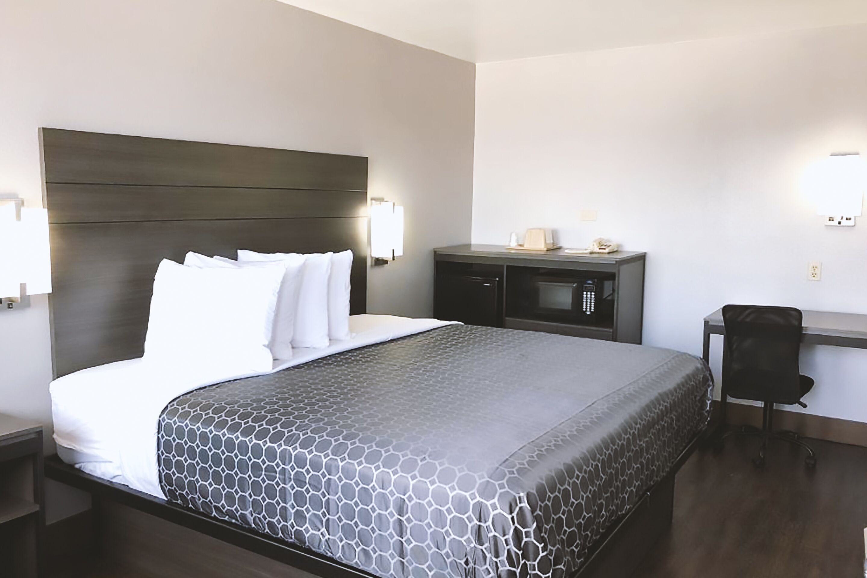 A hotel room with a large bed, a desk, a chair, a microwave, and a nightstand.