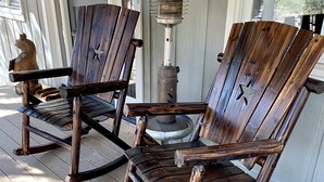 Zwei Schaukelstühle auf einer Holzterrasse mit einem Metallheizgerät und einem Willkommensschild.