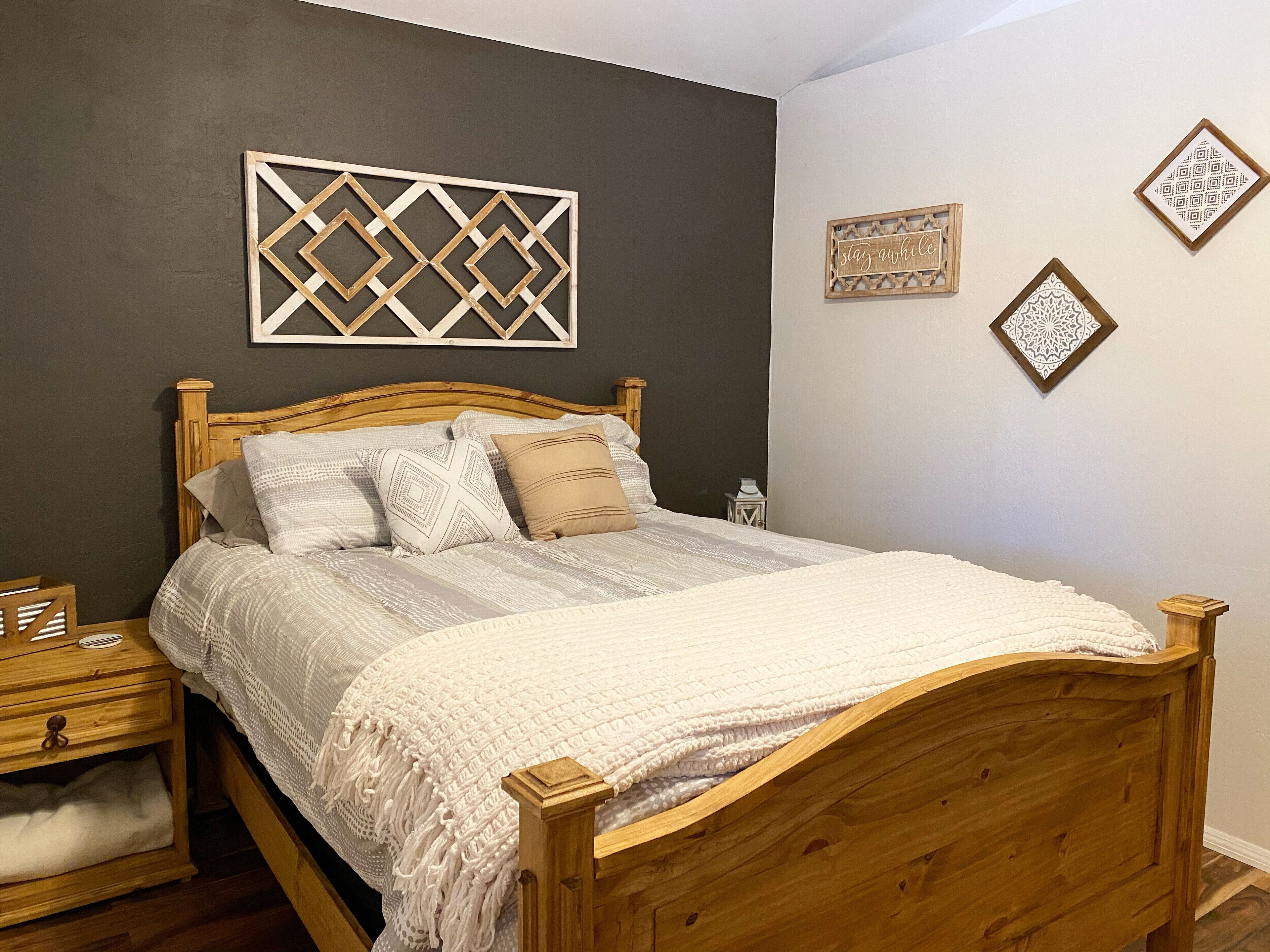 A wooden bed with a white comforter and pillows, a wooden nightstand with a lamp, and decorative wall art.