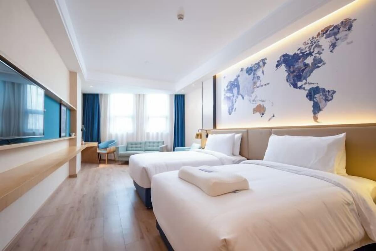 Ein Hotelzimmer mit zwei Betten, einer Weltkarte an der Wand, einem Schreibtisch und einem Sessel.